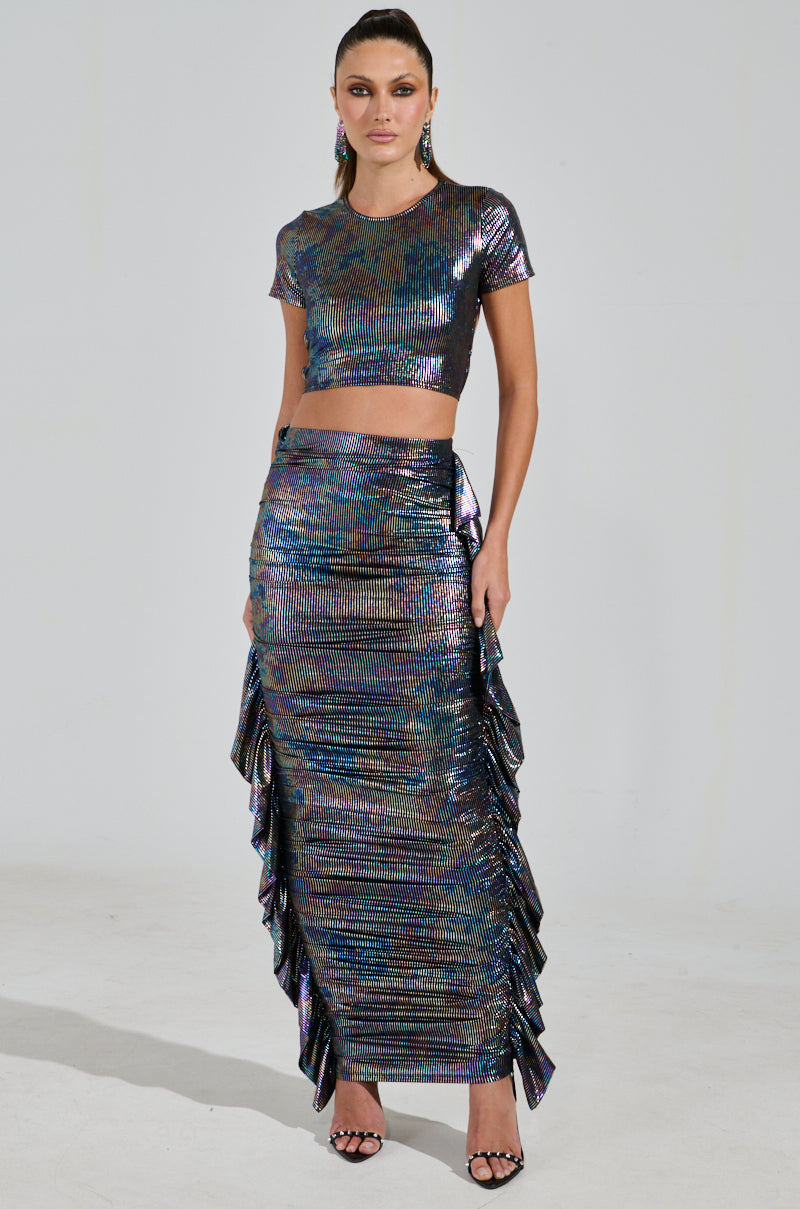 The person sports a shimmering, iridescent striped two-piece outfit with the ZEON TANK WITH TIE IN BACK and a floor-length ruffled skirt, standing against a plain background in high-heeled sandals.