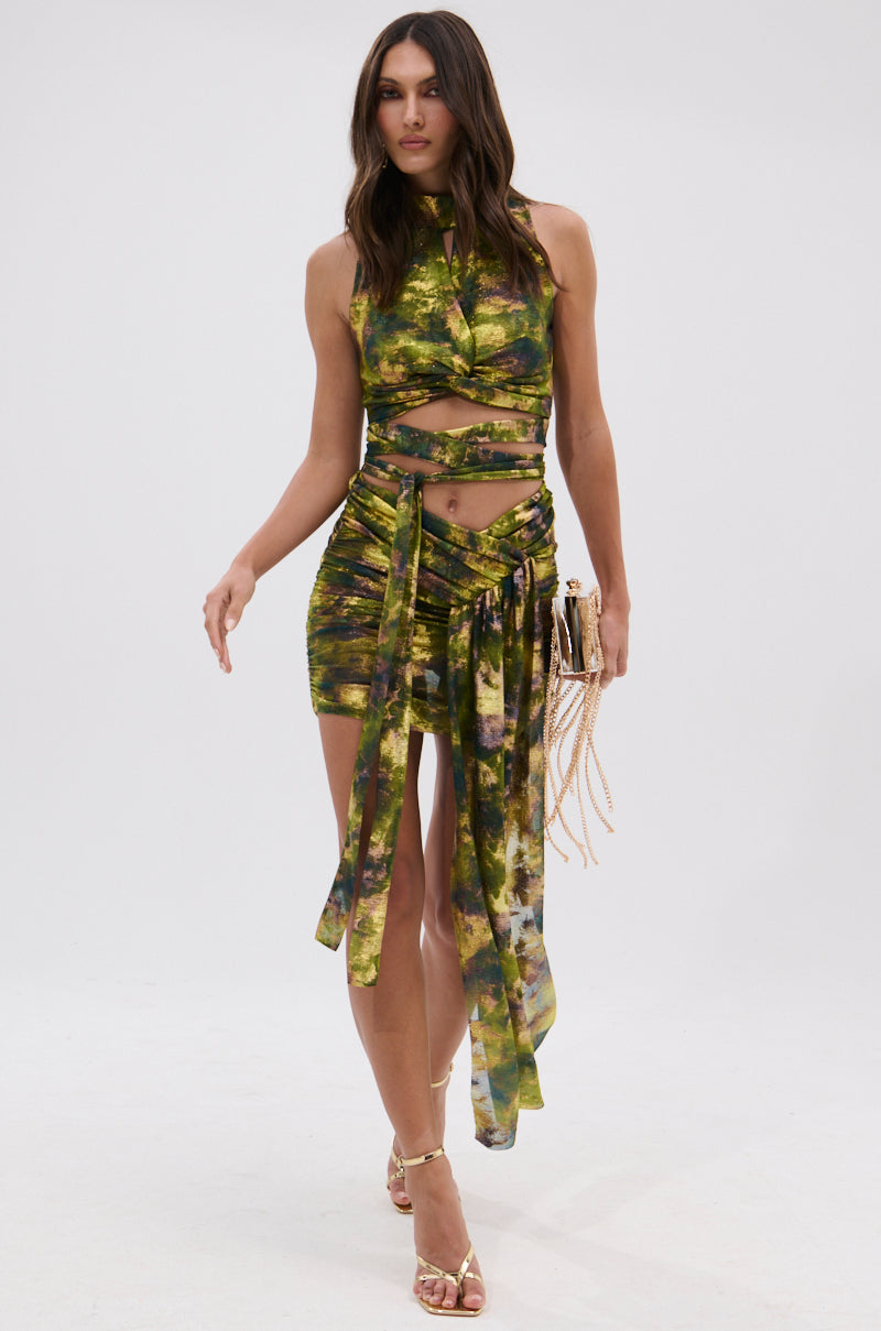 A woman walks forward wearing a sleeveless, tie-dye green and yellow crop top paired with the SEXY CAN I MINI SKIRT, holding a small gold handbag and wearing gold high-heeled sandals. 8