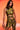 A woman with long, wavy dark hair stands against an orange background, confidently wearing the SEXY CAN I MOCKNECK BLOUSE WITH CUTOUT and a matching skirt, holding a gold purse.