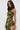 A woman with long brown hair wears the SEXY CAN I MOCKNECK BLOUSE WITH CUTOUT, styled as a cropped sleeveless top with abstract green and yellow patterns. She holds a gold chain purse and stands against a plain light background.