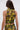 A woman with long brown hair is seen from behind, wearing the SEXY CAN I MOCKNECK BLOUSE WITH CUTOUT—a fitted sleeveless cropped top in a green and gold abstract pattern featuring a keyhole neckline.
