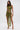 A woman stands against a plain white background wearing the SEXY CAN I MOCKNECK BLOUSE WITH CUTOUT, an abstract green and yellow cropped sleeveless top with a matching high-slit skirt, accessorized with a gold chain bag and gold heels.