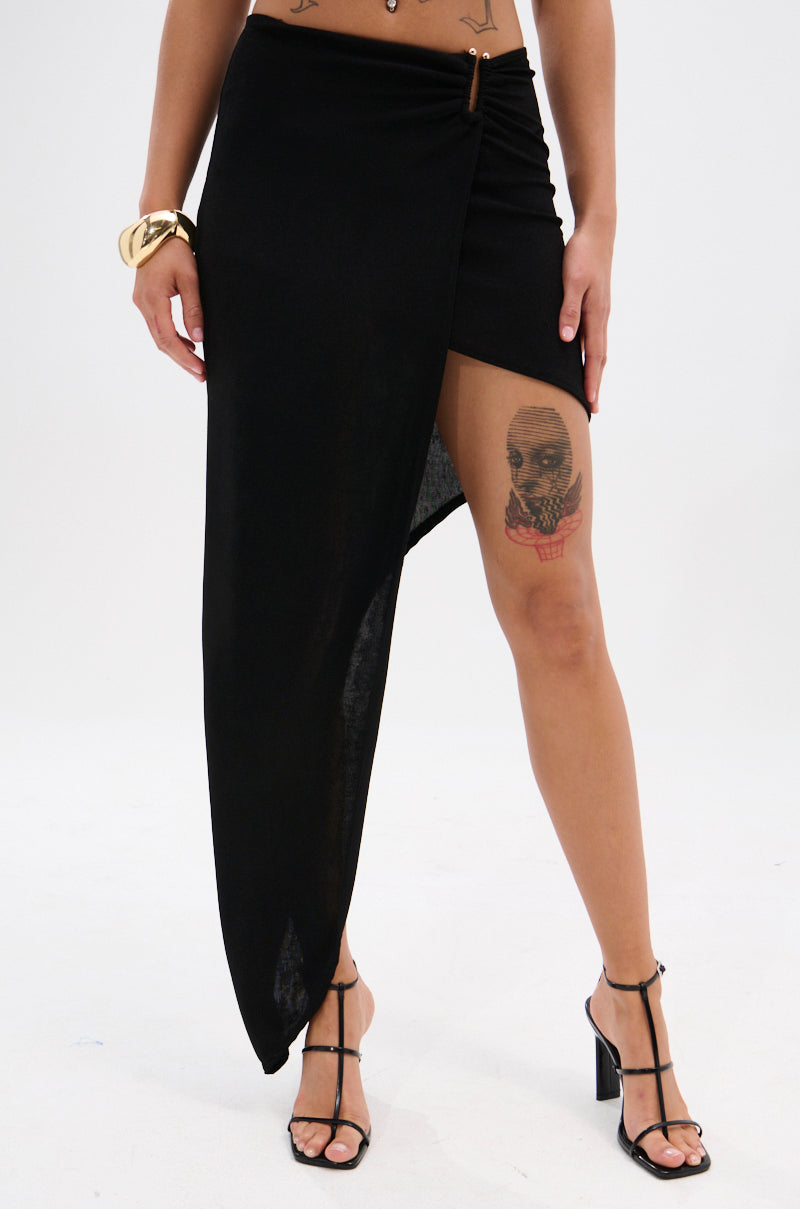 A person wearing the KYLIE SLINKY MIDI SKIRT, black strappy heels, a gold bangle, and displaying a detailed skull tattoo on their right thigh.