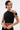 A person with short dark hair, piercings, and tattoos wears the KYLIE SLINKY OFF THE SHOULDER BLOUSE, a black stretch-knit crop top with a metal ring detail, accessorized by large hoop earrings and gold bracelets.
