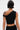 A person with short black hair and a blonde streak wears the KYLIE SLINKY OFF THE SHOULDER BLOUSE in stretch-knit, shown from the back with visible arm and shoulder tattoos against a plain, light-colored background.