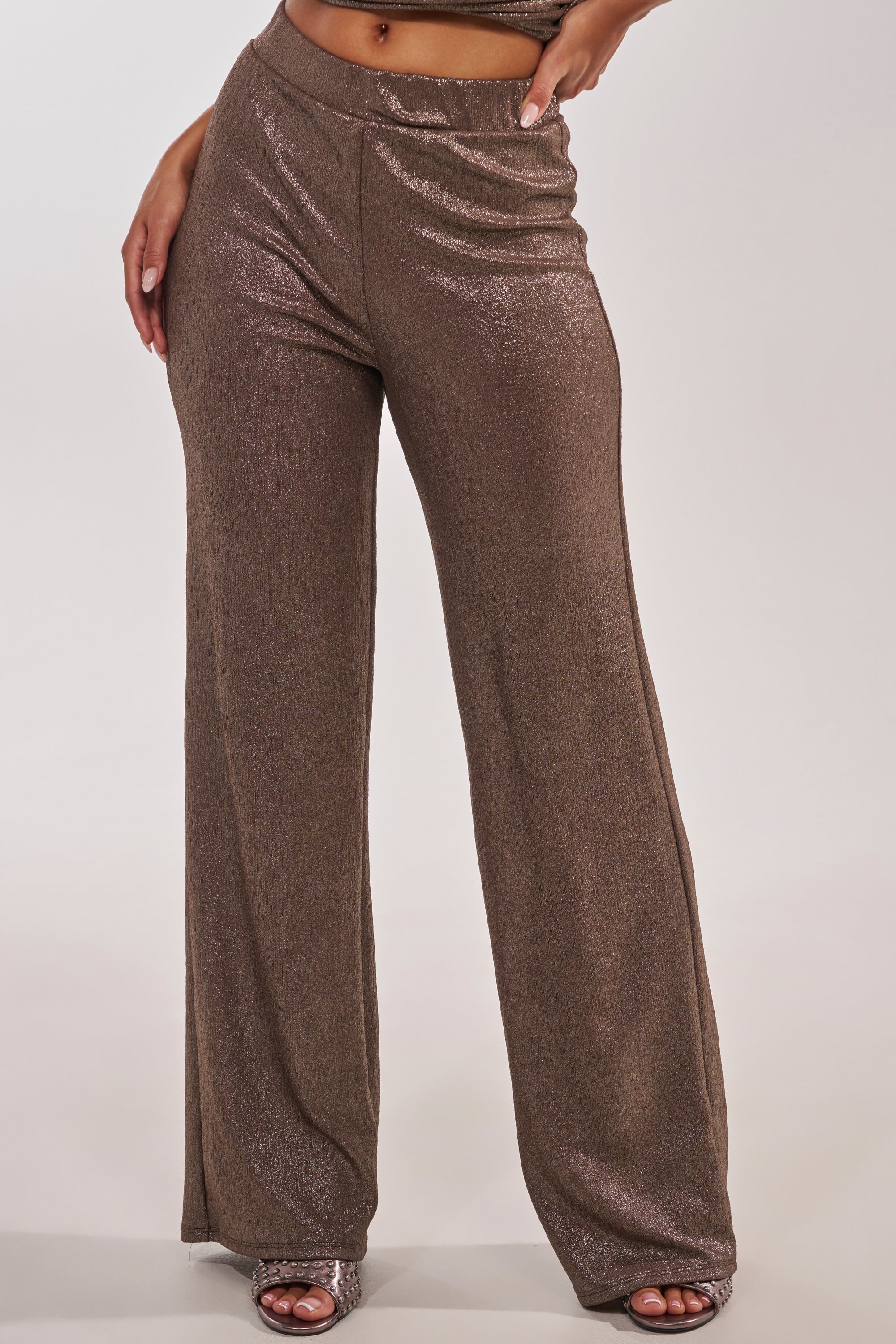 Wearing the HIGH STAKES RELAXED PANT with a sparkly, shimmery wide-leg design and open-toe heels, a person poses confidently, one hand on their hip against a plain background. 0