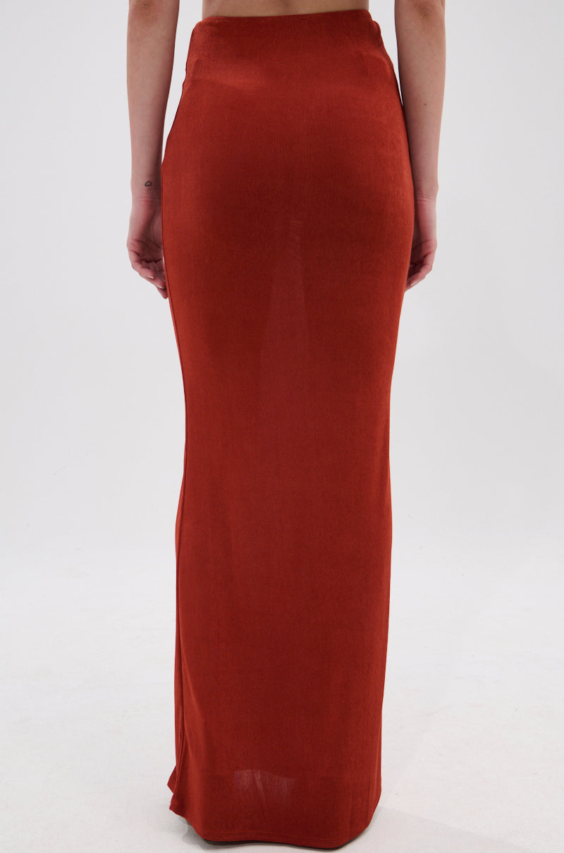 A person is shown from the waist down wearing the ON MY MIND SLINKY MAXI SKIRT in rust, featuring a high-rise waist and floor-length fit against a plain white background. 3