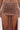 A close-up of a person wearing the DAYDREAMING SLINKY HIGH LOW SKIRT in light brown, featuring a high-waisted fit, ruched details, and two high slits revealing the upper thighs against a plain white background.