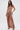 A woman wears the DAYDREAMING SLINKY HIGH LOW SKIRT—a light brown, high-waisted ruched skirt with thigh-high slits—paired with a matching fitted crop top, long wavy hair, gold jewelry, and black strappy high-heeled sandals.