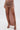 A person wearing the DAYDREAMING SLINKY HIGH LOW SKIRT, a ruched light brown skirt with two high front slits, paired with strappy black sandals against a plain white background.