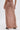 A person wearing the DAYDREAMING SLINKY HIGH LOW SKIRT, a long, fitted light brown skirt with ruched back detailing, is standing on a white background. Only the lower half of their body is visible.