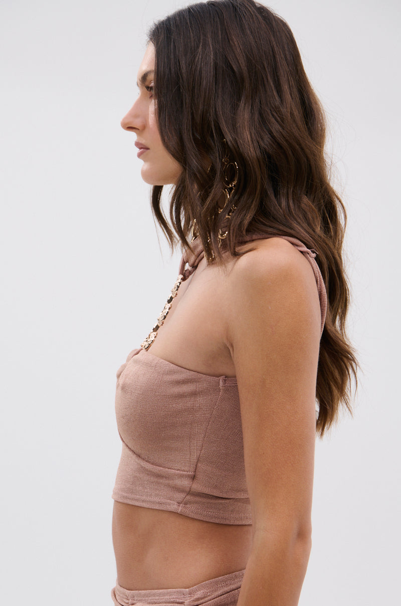 A woman with long, wavy brown hair stands in profile against a plain light background, wearing the DAYDREAMING SLINKY HALTER BLOUSE featuring a gold chain neckline, matching bottoms, and accessorized with gold earrings and a necklace. 7