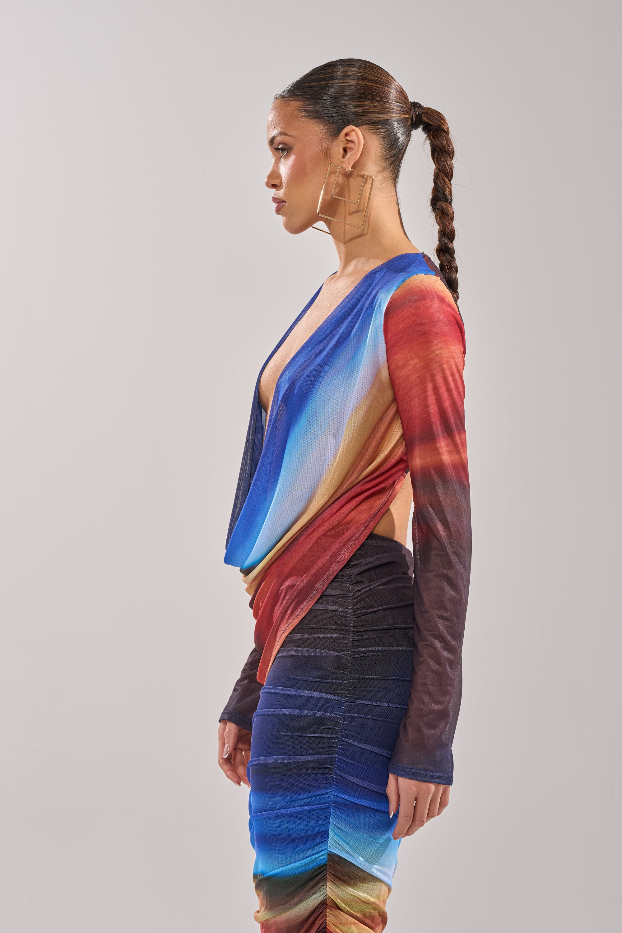 A woman with braided hair, large square earrings, and a long-sleeved BOOM BOOM MESH BLOUSE with a deep neckline stands in profile against a plain light background. 3