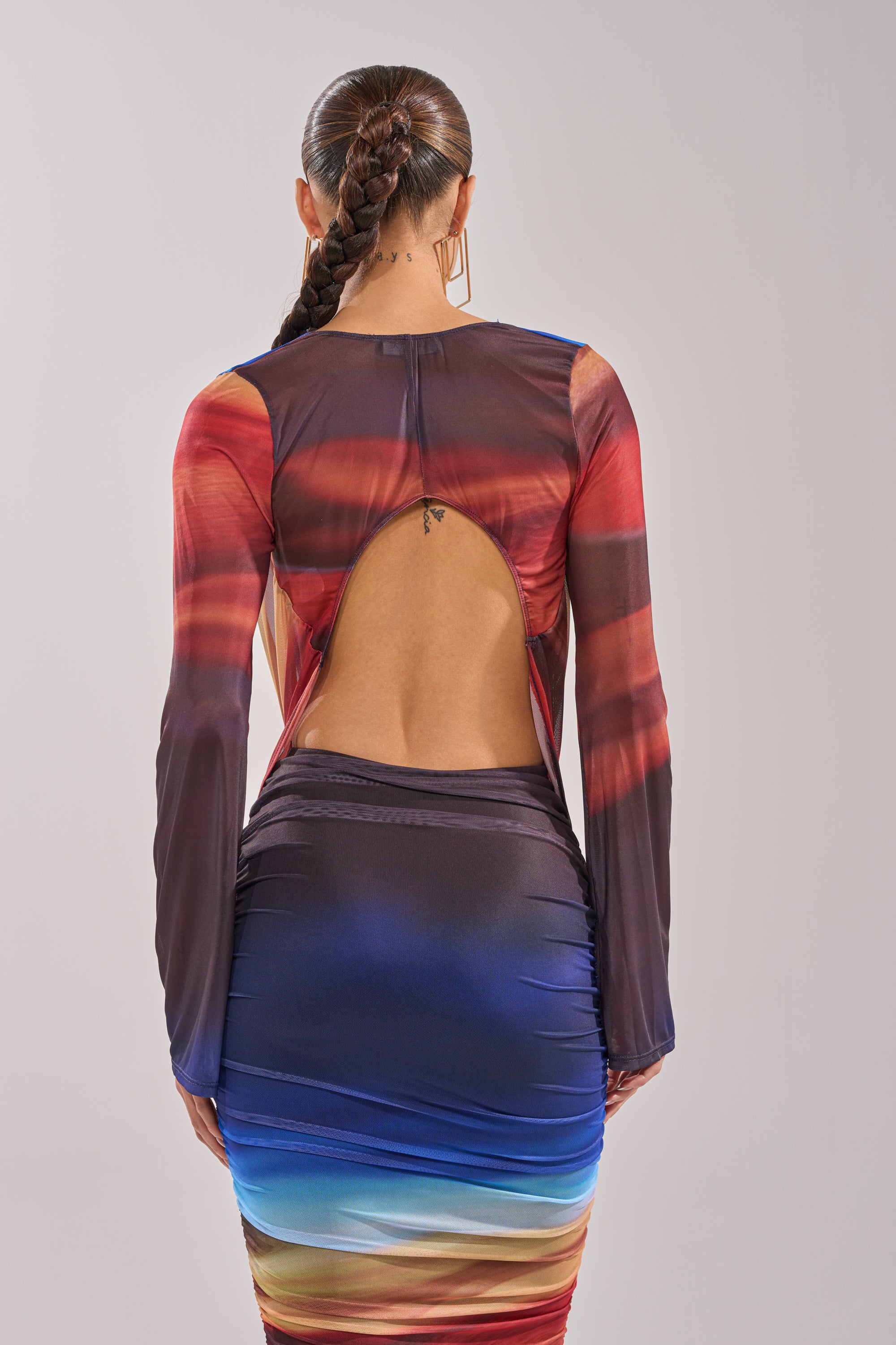 A woman with a long braid wears the BOOM BOOM MESH BLOUSE, a fitted, multicolored ombre mesh top featuring long sleeves and an open back, standing against a plain light background. 4
