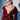 A woman with short, slicked-back hair wears a glossy red trench coat styled with the LOVER GROMMET PU BELT. She poses confidently against a light background with dramatic shadows.