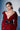A woman with short, slicked-back hair wears a glossy red trench coat styled with the LOVER GROMMET PU BELT. She poses confidently against a light background with dramatic shadows.