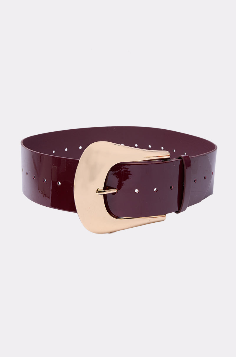 The CINCH IT UP BELT is a wide, glossy dark burgundy faux patent leather belt with a large shiny gold buckle, shown against a plain light gray background.