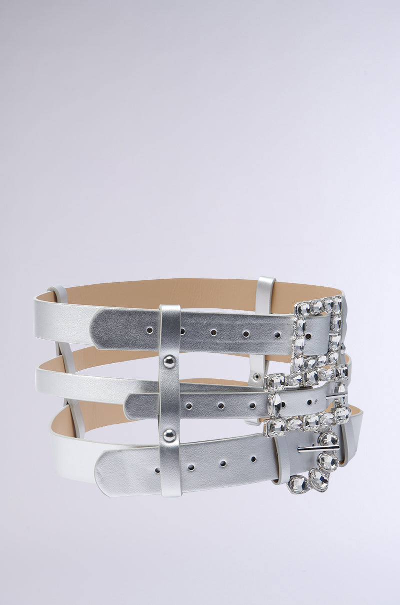 The GET ON MY LEVEL MULTI BUCKLE BELT is a contemporary waist accent crafted from white faux leather, featuring three parallel straps and an eye-catching jeweled buckle. Its chic design is set off by subtle metallic silver undertones against a simple gray background. 3