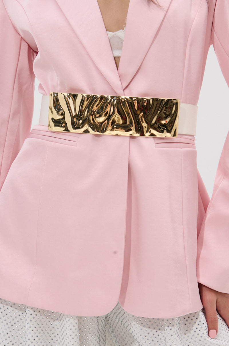 A person wears a light pink blazer cinched at the waist with the BOUJEE PU STRETCH BELT. The outfit is finished with white pants that have small silver embellishments.