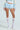 Person in a light blue sweater, SHAKE IT BABY RUFFLE SHORT IN BABY BLUE bloomers, white knee-high lace socks with bows, and white high-heeled shoes, set against a plain background.