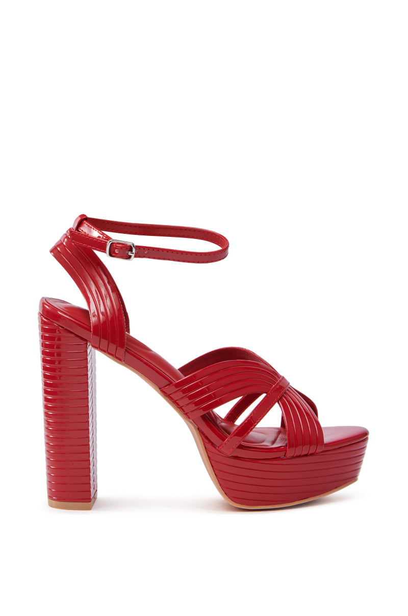 The AZALEA WANG RED STRAPPY PLATFORM SANDAL is a red high-heeled sandal made from faux leather, featuring a strappy design, adjustable ankle strap, platform sole, and chunky block-style heel with a textured finish.