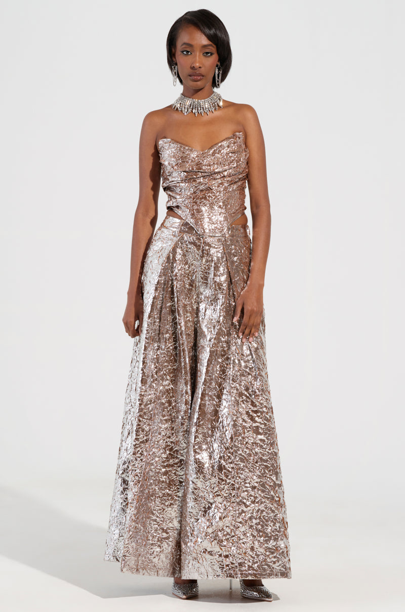 Dressed in the STAR PANT, a woman showcases a strapless gown with a dazzling metallic silver hue and textured, crinkled design. She complements her ensemble with a matching choker necklace and elegant high heels, enhancing its sophisticated allure. Her attire evokes the glamour of metallic pants against the plain white background. 0