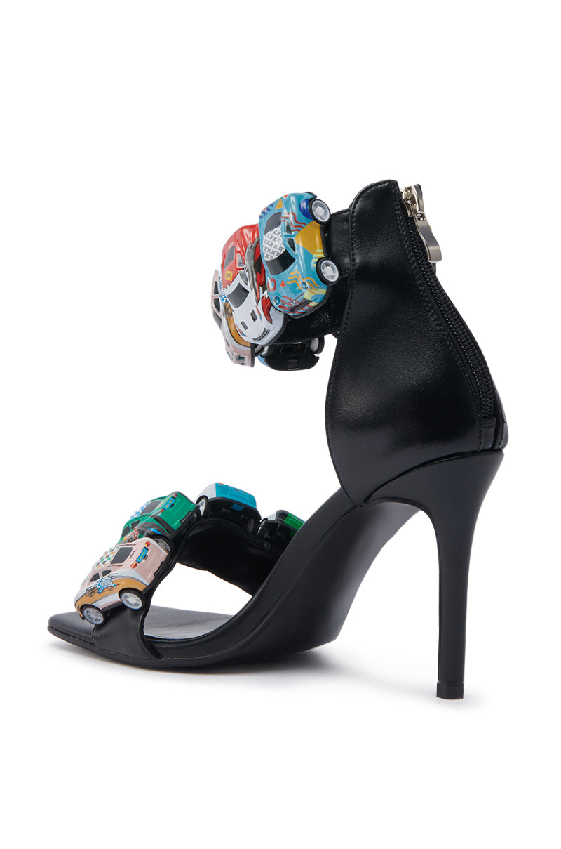 The AZALEA WANG STARLITE BLACK CARS STILETTO SANDAL is a black faux leather sandal with an open square toe, back zip closure, and colorful toy cars on the front and ankle straps.
