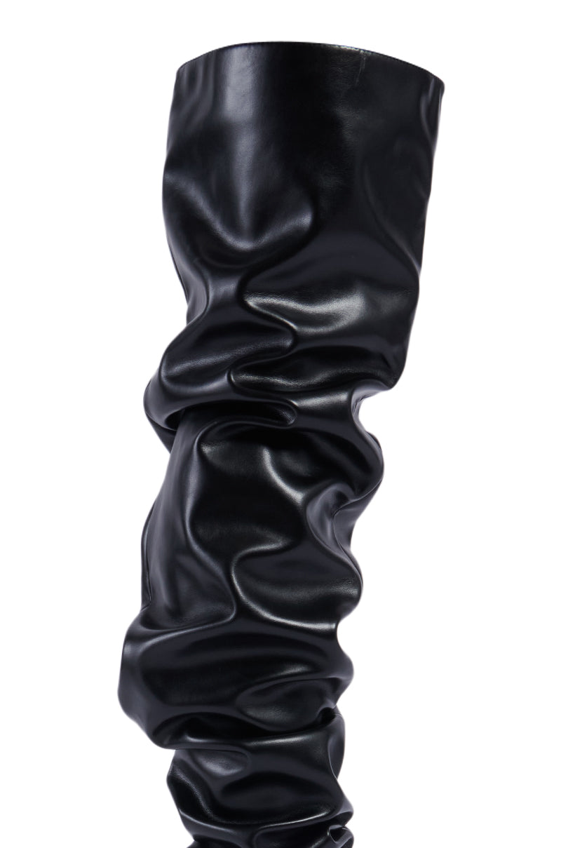 The AZALEA WANG STEPHAN BLACK BOOT is a striking, thigh-high boot crafted from shiny, crinkled leather material. It features a ruched texture that creates elegant folds and wrinkles along its length, offering a unique and stylish appearance.