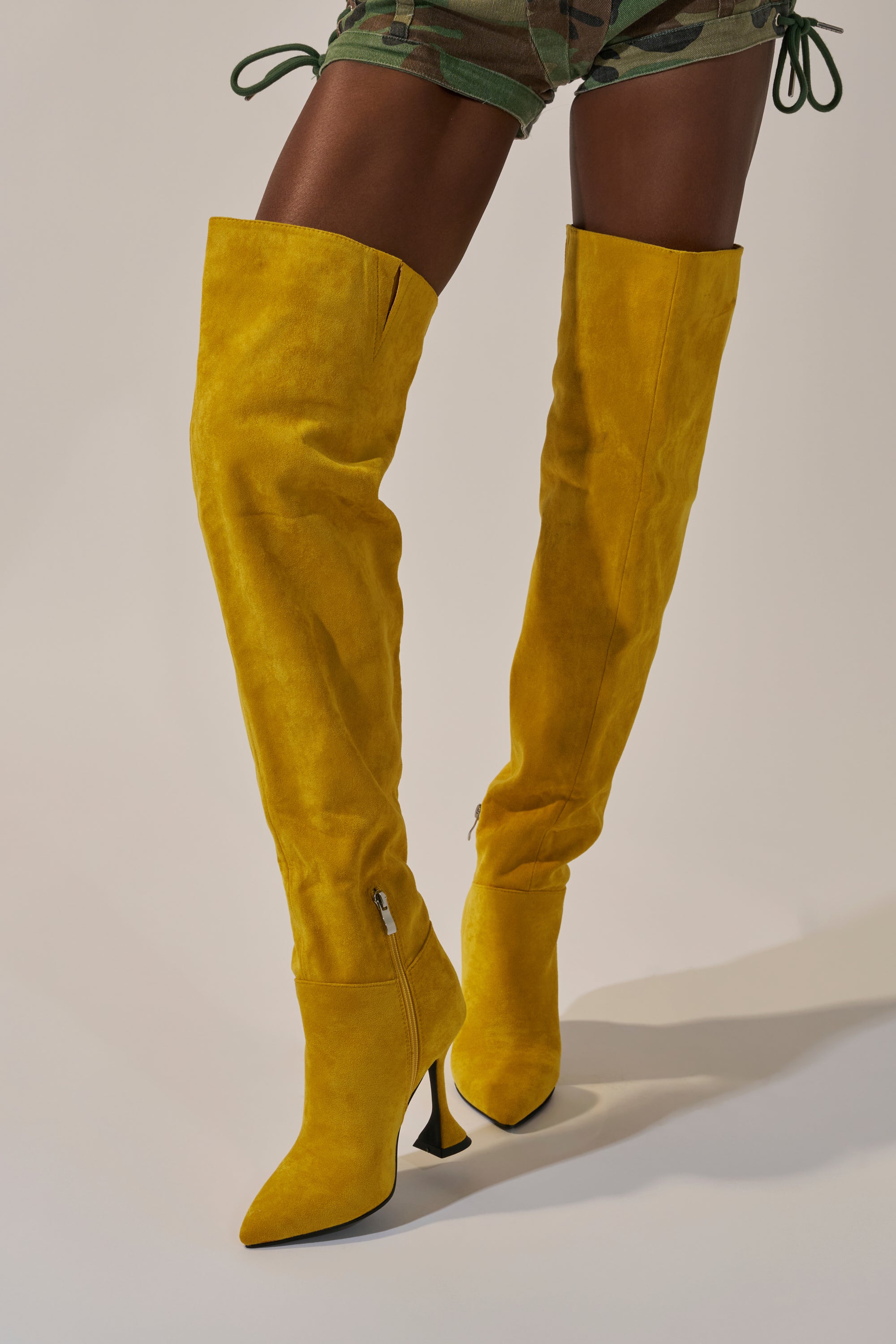 A person wears the AZALEA WANG STEPHAN YELLOW SUEDE CHUNKY BOOT with camouflage shorts, standing on a light-colored background.