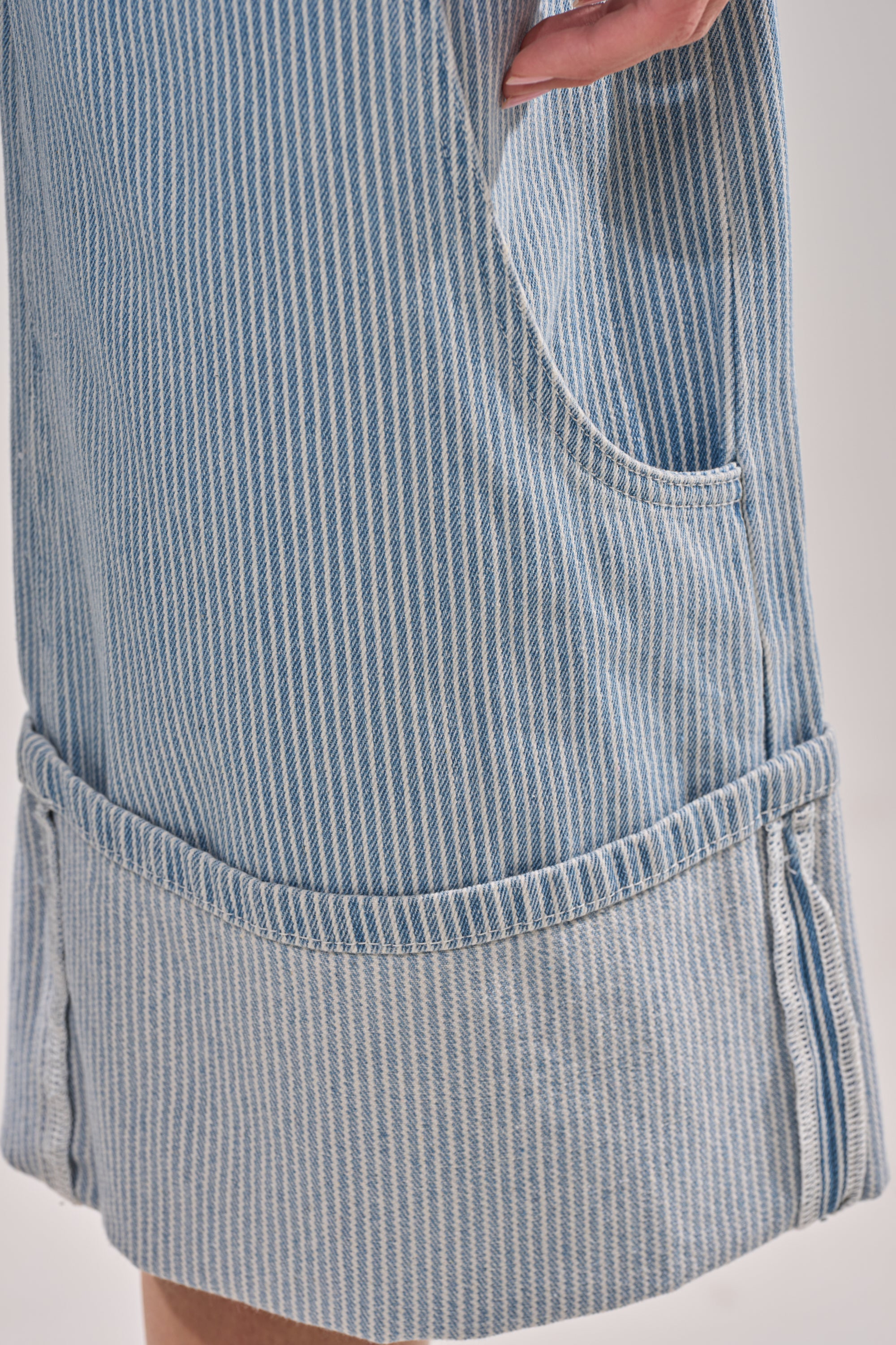 Close-up of the FEEL FREE STRIPE GAUCHO: vintage-inspired blue and white striped denim bermuda shorts, with a large pocket, wide folded cuff, and mid-rise fit. A hand partially in the pocket showcases its stylish design. 9