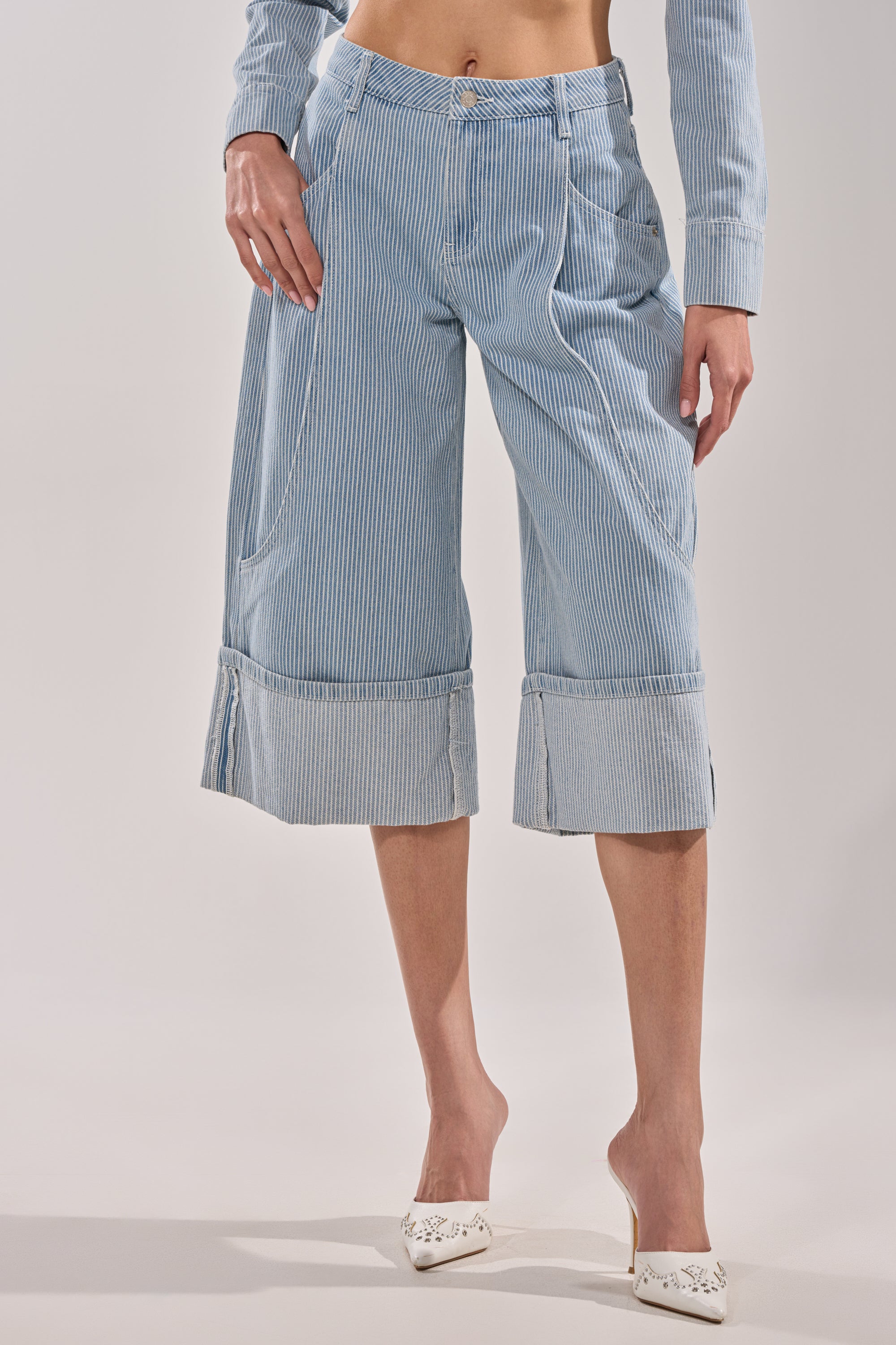 A person wears the FEEL FREE STRIPE GAUCHO—light blue, pinstriped, wide-leg cropped pants with a matching top—styled barefoot on one foot and a white pointed-toe shoe on the other for a vintage vibe. 2