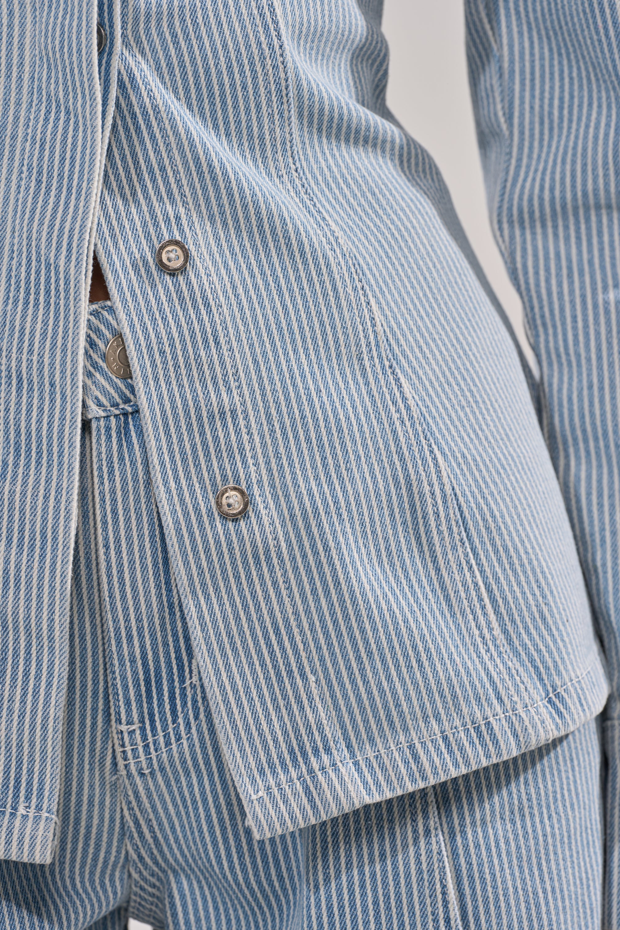 Close-up of a person wearing the FEEL FREE STRIPE BUTTON DOWN, a blue and white striped denim-like blouse with a collar and partially unbuttoned front, paired with matching pants. 11