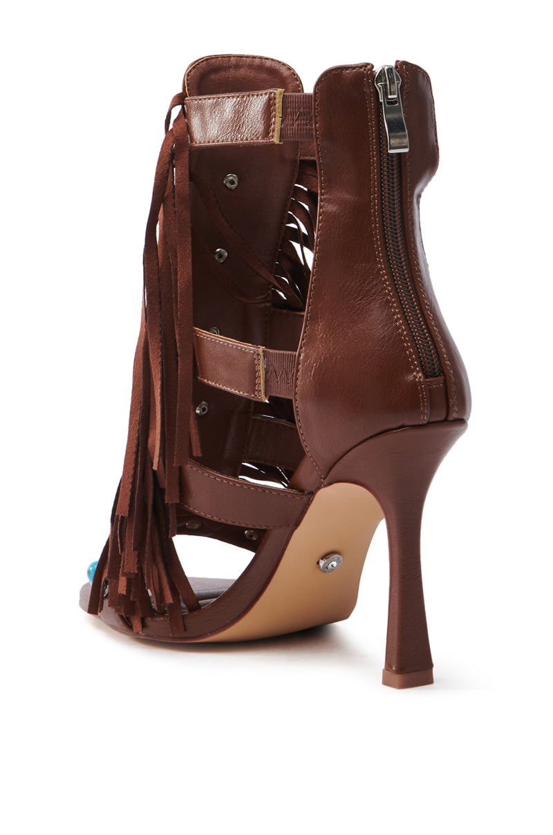 The AZALEA WANG SUMAC BROWN WESTERN SANDAL is a brown gladiator-style sandal with fringe detail and a back zipper, crafted from faux leather. It features cut-out straps, a stiletto heel, and visible stitching.