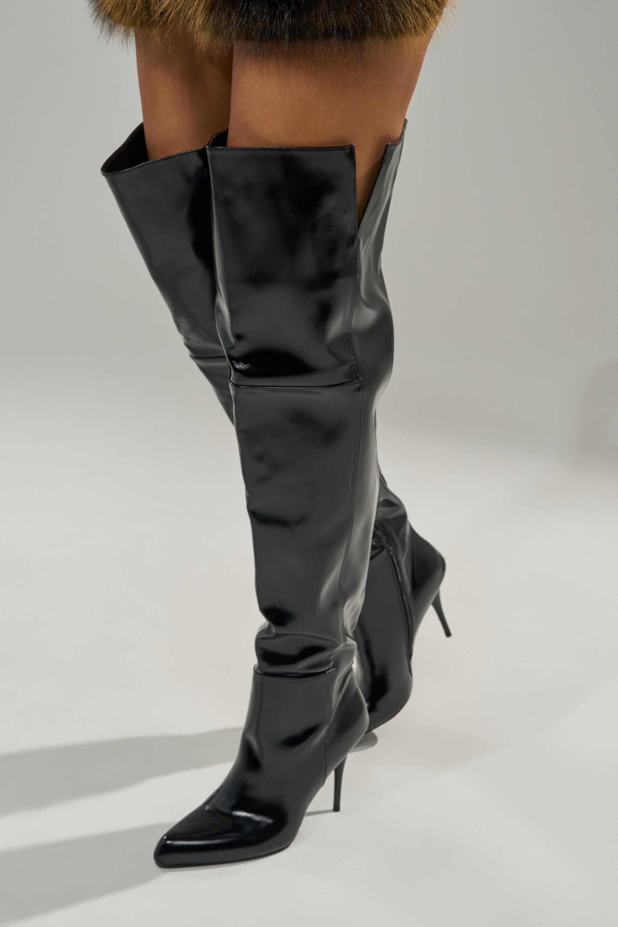 A person models the AZALEA WANG SUNSHINE THIGH HIGH BLACK PU STILETTO BOOT, standing on a light gray surface with only the lower half of their legs visible.