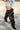 A person wearing distressed denim shorts and AZALEA WANG SWELCIE Chocolate Brown Folded and Snap Detail Thigh High Boots stands on a city street.