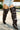A person stands outdoors on a sunny day wearing distressed denim shorts and the AZALEA WANG SWELCIE Chocolate Brown Folded and Snap Detail Thigh High Boot with stiletto heels.