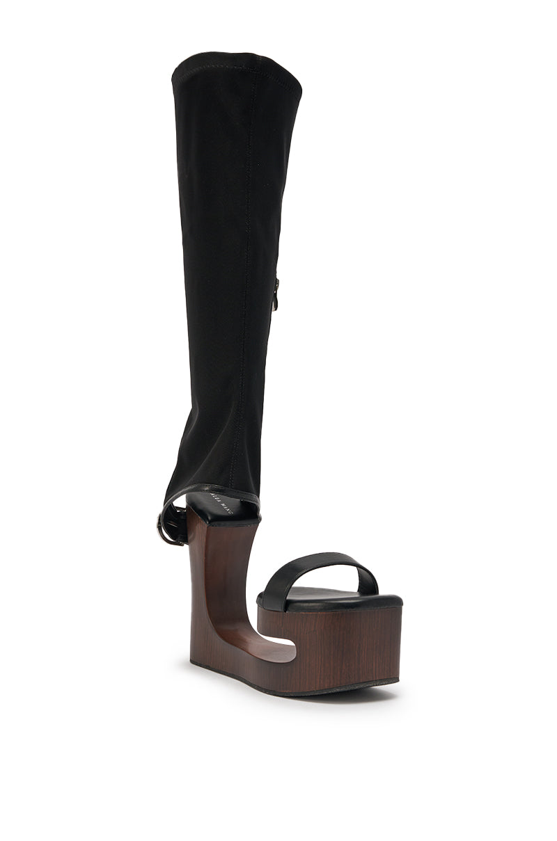The AZALEA WANG SWINDLE BLACK NOVELTY WEDGE SANDAL features a thick wood-like platform, open toe, black strap, and a tall black fabric leg covering that extends above the ankle. 4