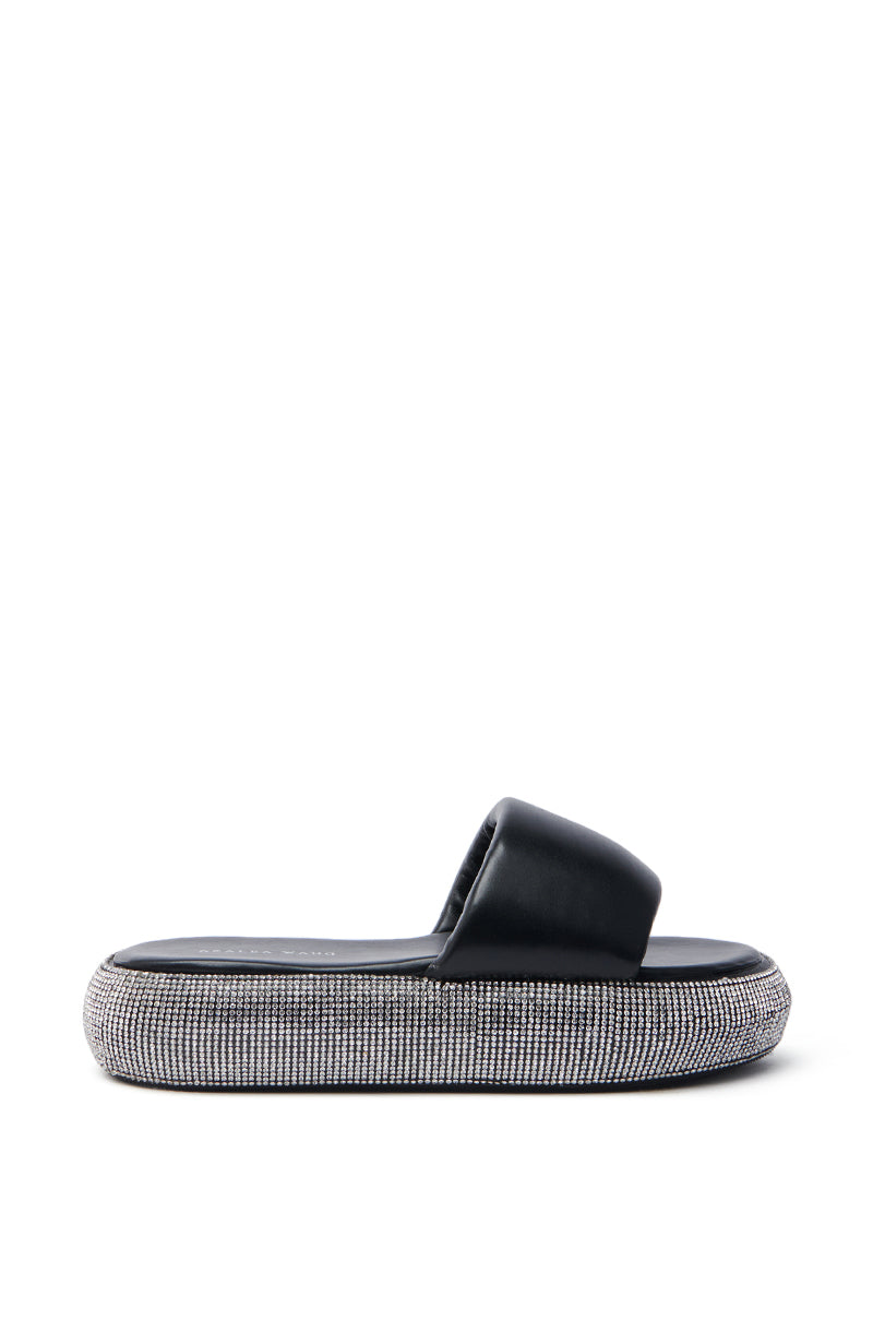 The AZALEA WANG SWITZERLAND BLACK RHINESTONE SANDAL is a vegan leather black slide with a thick cushioned strap and a rhinestone-embellished flatform sole, set against a white background.