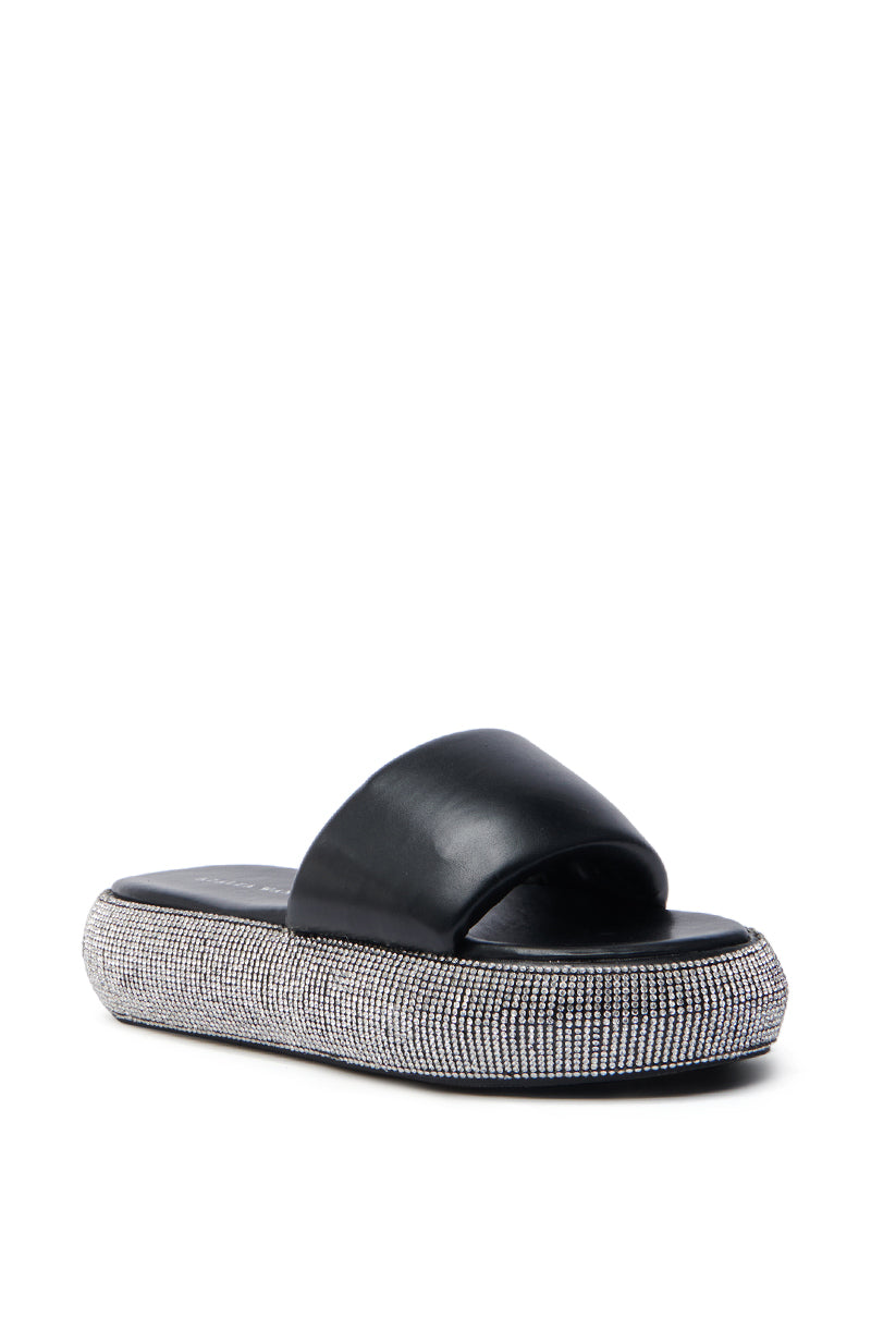The AZALEA WANG SWITZERLAND BLACK RHINESTONE SANDAL showcases a black slide design with a wide strap and a sparkling rhinestone-encrusted flatform sole, offering casual comfort and modern elegance in vegan leather.