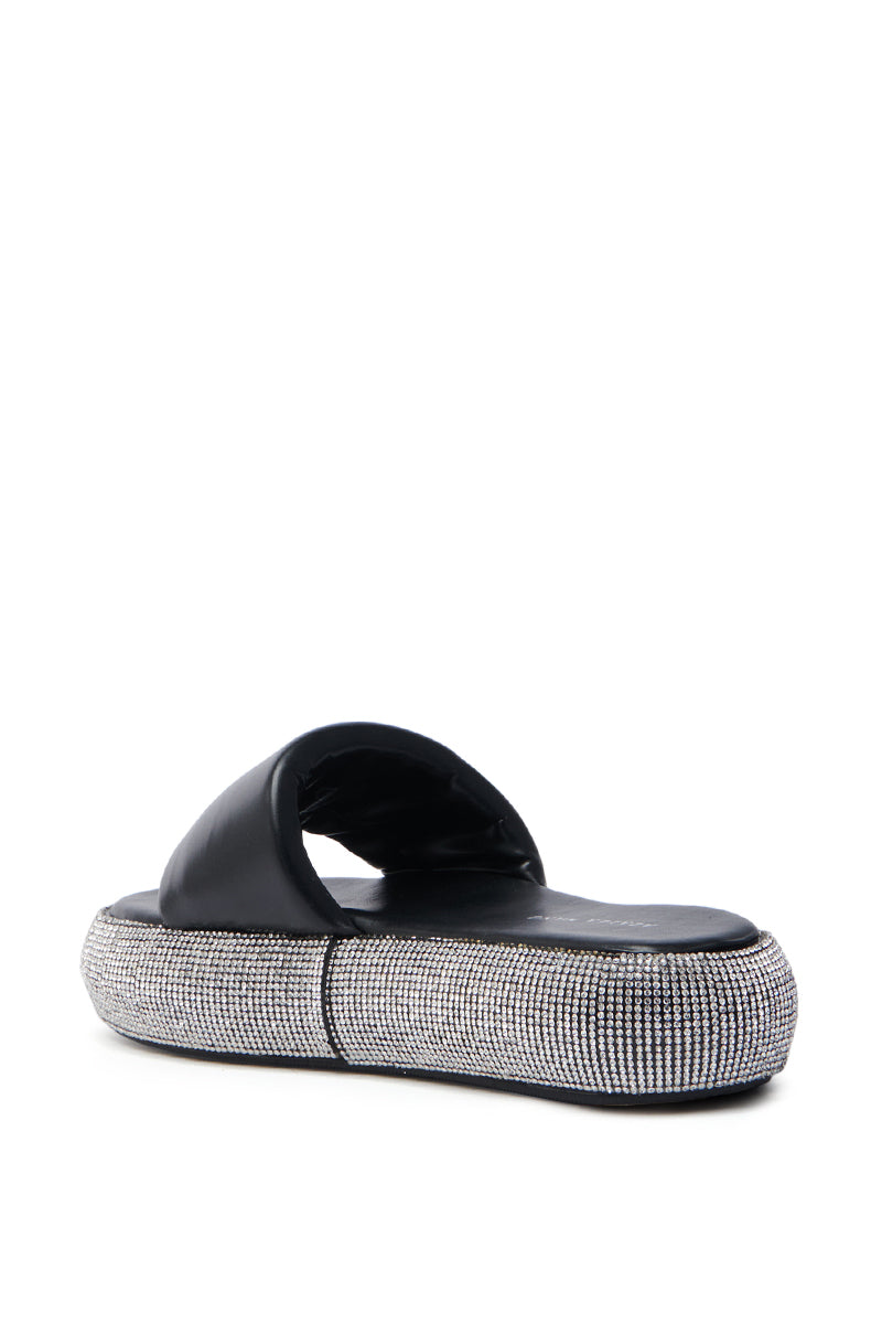 The AZALEA WANG SWITZERLAND BLACK RHINESTONE SANDAL features a wide strap, a flatform sole, and sparkling rhinestones on vegan leather, combining style and sustainability.