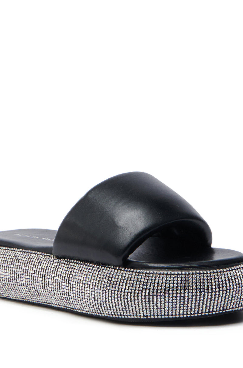 The AZALEA WANG SWITZERLAND BLACK RHINESTONE SANDAL features a close-up of its wide vegan leather strap and thick flatform sole, both embellished with sparkling rhinestones against a white background.