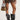 A person is wearing a black mesh-like dress with diamond-shaped patterns, the AZALEA WANG SYBEL BUTTON FLAT BOOTIE, which are oversized mid-calf boots featuring thick platform lug soles. They accessorize with a small camouflage handbag and multiple silver bangles on their wrists. The background is plain off-white.