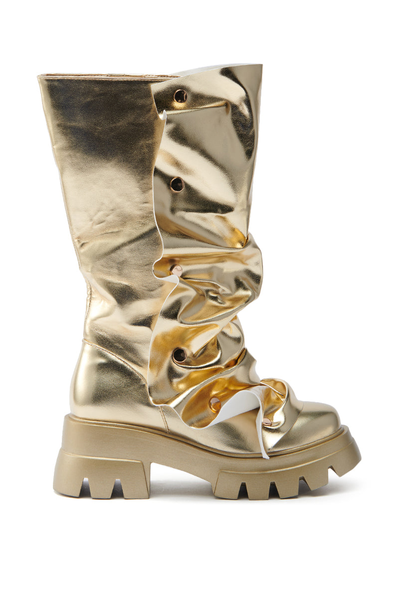 The AZALEA WANG SYBEL BUTTON GOLD FLAT BOOTIE is a metallic gold faux leather boot with a chunky platform lug sole and heel. It has large eyelets and gathered detailing down the front for a ruched effect, with a bold, glossy design that reflects light beautifully.