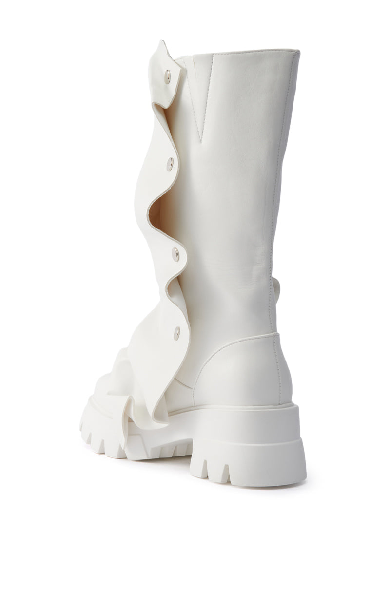 The AZALEA WANG SYBEL WHITE SNAP DETAIL BOOTIE features white faux leather, a chunky platform lug sole, bold wavy ruffle side detail, and decorative snap buttons, shown in a three-quarter rear view on a white background.