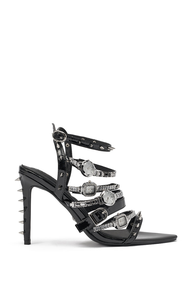 The AKIRA GOLD SYDONIC BLACK WATCH STILETTO SANDAL is a black faux patent leather sandal with spiked hardware, rhinestones, silver buckle straps, and spike accents on the back of the heel and ankle straps. 5