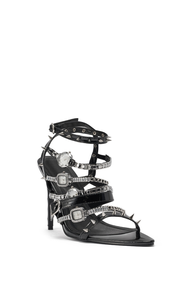 The AKIRA GOLD SYDONIC BLACK WATCH STILETTO SANDAL is a high-heeled black faux patent leather sandal with stiletto heels, multiple straps, silver buckles, spiked hardware, and rhinestone accents for an edgy punk-inspired look. 6