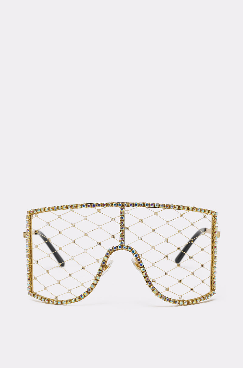 The POP THE BUBBLY GLASSES IN GOLD feature a gold metallic frame, a single visor-style lens with diamond-patterned mesh, multicolored jewels, a rhinestone outline for extra sparkle, and black arms on a white background. 0
