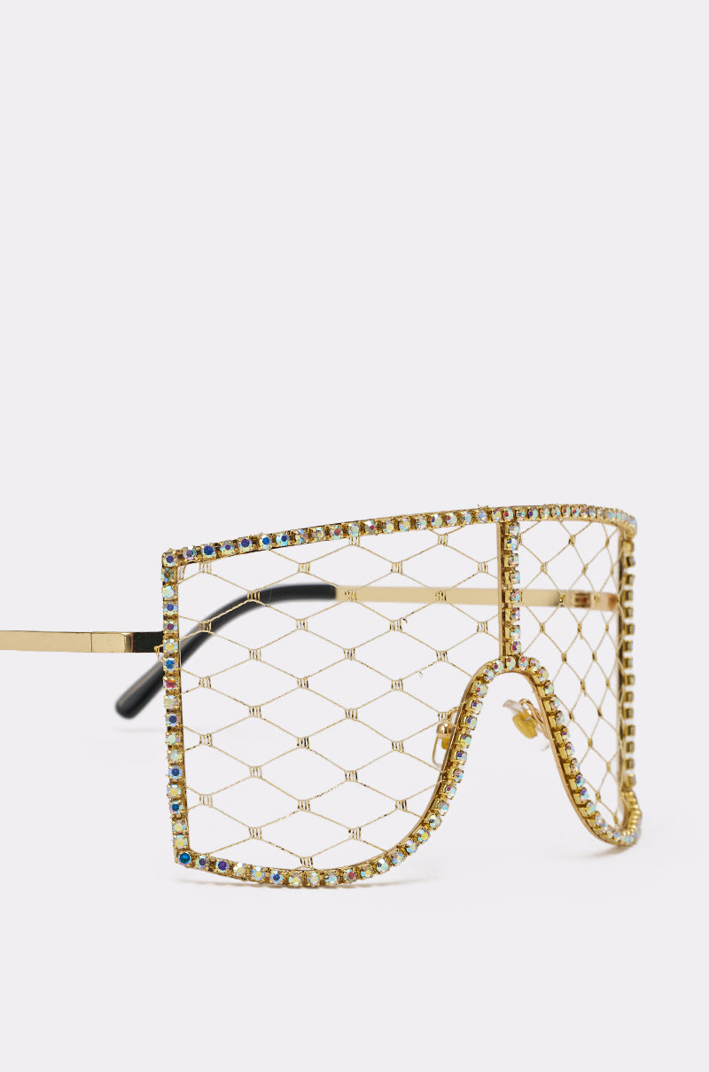 POP THE BUBBLY GLASSES IN GOLD are oversized gold visor-style sunglasses featuring a lattice wire mesh and sparkling multicolor rhinestones around the frame, shown against a plain white background. 3