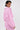 A woman with short dark hair poses in the BUBBLEGUM BUBBLE HEM BOMBER, a textured light pink coat with a belted waist and large collar. She turns slightly to the side, looking over her shoulder against a plain light background.