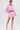 A woman poses confidently in the BUBBLEGUM BUBBLE HEM BOMBER, styled with a matching mini skirt and pink platform heels. Her slicked-back hair and visible thigh tattoo stand out against the plain white background.